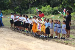 Nursery and Primary School students stand with their teachers as they wave the flags of Guyana and England before the arrival of Prince Harry
